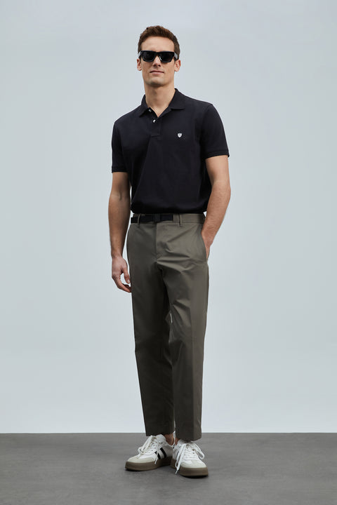 Man wearing a black polo shirt, dark gray pants, and white sneakers against a light gray background